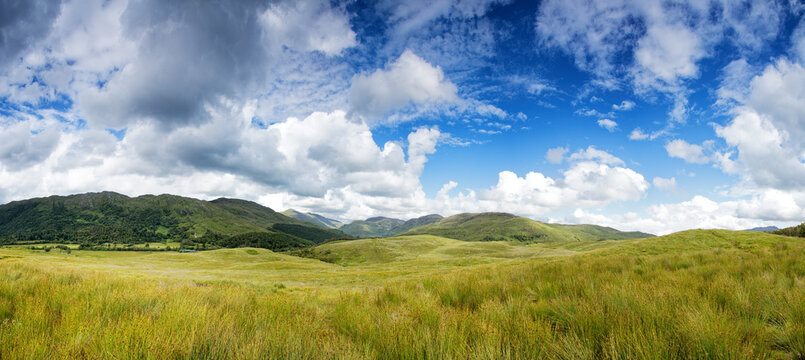 Panorama of the Scottish Highlands with button grass in the foreground and the rolling mountains with a summer sky behind