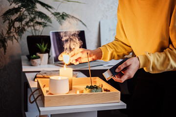 Fototapeta na wymiar Meditation, relaxation after work. Woman getting ready meditating and lights up indian incense stick and candles. Woman hands with Smoke indian incense stick, burning candles on the table at home