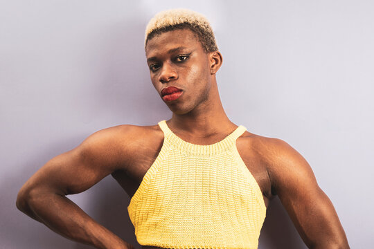 An androgynous black man posing on a purple studio background in makeup.