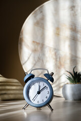 Blue alarm clock on table on wooden background with natural shadows, new day beginning concept, vertical