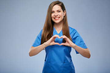 Young nurse woman in blue medical suit makes heart shape figure with fingers. Isolated female...