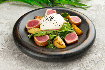 Salad with fried tuna in a plate on a gray background.