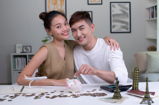 Portrait of Young Asian couple plans to save money for a trip around the world, looking at the camera.Travel budget concept, passport monument model and aircraft toy in the picture.