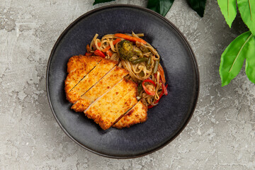 Fried chicken and wok noodles in a plate. on a gray background.
