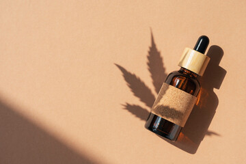 Amber bottle with cannabis oil used for medical purposes on beige background with daylight and the...