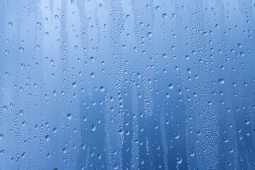 Close-up of raindrops on a window pane. Gloomy wet weather. Drops of water on glass in front of dark blue rain clouds. Rain. Abstract background texture. Wallpaper.