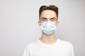 Young man wearing medical mask with eyes wide open studio shot on gray background