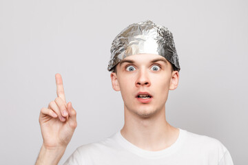 Paranoid young man wearing tin foil hat pointing up studio shot on gray background