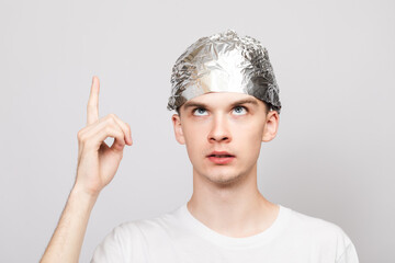 Paranoid young man wearing tin foil hat pointing up studio shot on gray background
