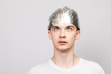 Paranoid young man wearing tin foil hat studio shot on gray background