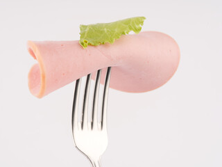 Sausage on a fork with a lettuce leaf. Closeup. On a white background.
