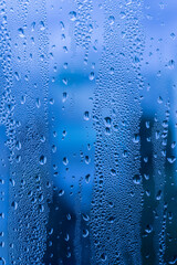 Close-up of raindrops on a window pane. Gloomy wet weather. Drops of water on glass in front of dark blue rain clouds. Rain. Abstract background texture. High quality photo