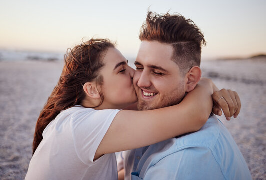 Love, couple and kiss on beach happy to celebrate relationship with sunset being relax, smile and on holiday. Romance, man and woman hug, embrace and bonding on seaside vacation together outdoor.