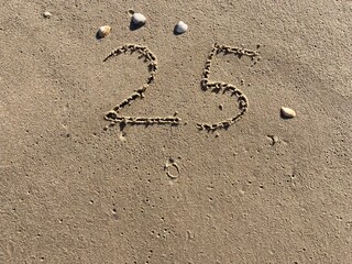 On the beach in the sand is carved the number 25