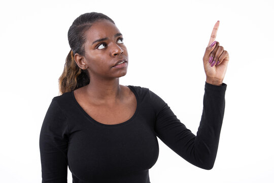 Portrait of serious African American woman pointing finger up. Worried young model in black shirt with ponytail looking away, showing something strange. Advertising concept.