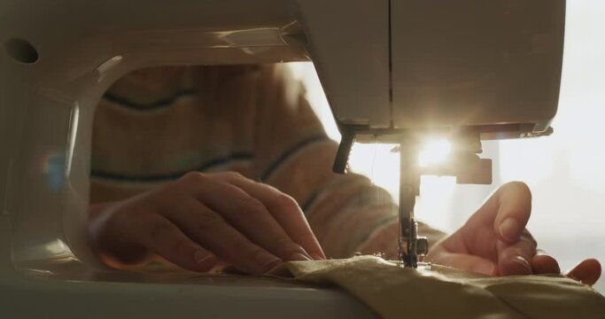 A woman sews bed linen on a sewing machine, close-up.