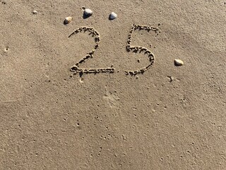 Fototapeta na wymiar On the beach in the sand is carved the number 25