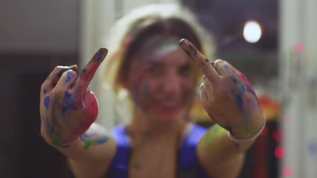 Portrait of a female artist. Girl with clumsy clorful painted face showing middle fingers.