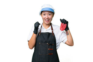 Young caucasian woman wearing an apron and serving fresh cut meat over isolated background celebrating a victory in winner position