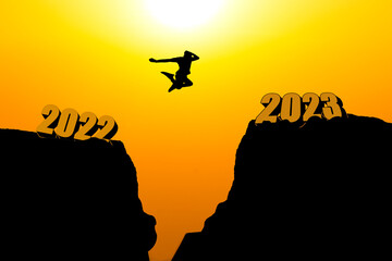 Human silhouette jumping over a cliff, skipping 2022 into 2023 on the background of a new morning, happy New year concept.