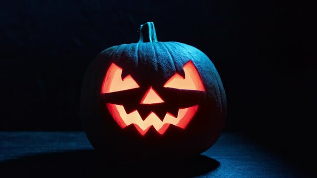 Halloween pumpkin with flashing eyes on dark background. Jack o' Lantern at night. Pumpkin with scary face. Halloween concept. 4K, UHD