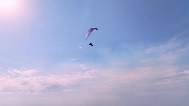 Aerial view of a paraglider with a wing and in a kokan flying a cruise in sunny weather against a blue sky. Air sports. Leisure