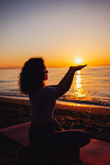 Young woman holding sun on hands, meditating near the sea