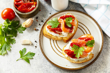 Open sandwiches or bruschetta with salted salmon, cheese and sun dried tomato on a stone table. Healthy food, seafood.
