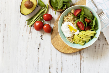 Keto diet. Delicious breakfast or brunch - poached egg, quinoa, avocado and fresh vegetable salad on the kitchen table. View from above. Copy space.
