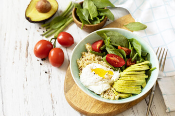 Keto diet. Delicious breakfast or brunch - poached egg, quinoa, avocado and fresh vegetable salad on the kitchen table. Copy space.