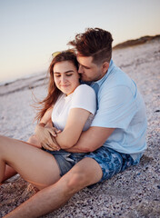 Couple, relax and hug for love on a beach sitting and enjoying time together in the outdoors. Young man hugging woman relaxing on a sandy ocean coast in Costa Rica for romantic relationship in nature