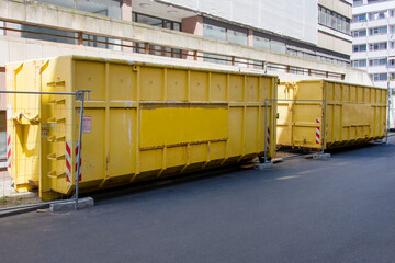 Yellow garbage containers near the building, construction site on the background. Recycling, construction waste, dumpster near construction site.