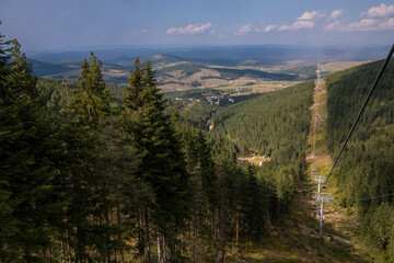Tourists sit in big suspended glass cabins riding to mountain peak. Scenic nature view. Cable car gold gondola lift is providing an aerial link over mountain Zlatibor in Serbia. 07.09.2022
