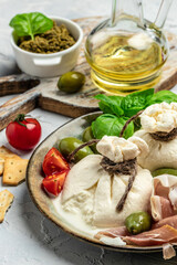 Italian burrata cheese with olives and cherry tomatoes, basil, olive oil on light background. top view