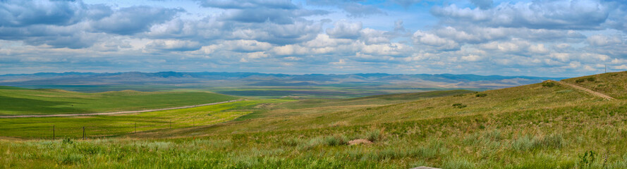 Bald Mountain in the Buryat Republic of Russia. Green hills against a blue sky with clouds.