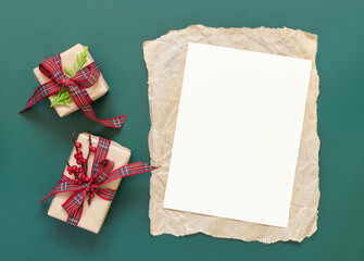 Blank paper card and wrapped Christmas presents on a green background top view