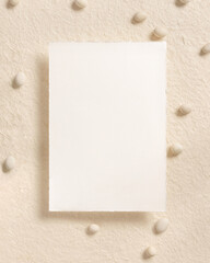 Blank card near pebble stones top view on beige, mockup. Romantic scene with vertical card