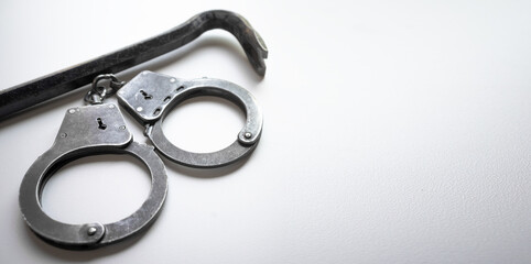 Metal handcuffs and a tire iron for opening the door on a white background. Burglary. Apartment...