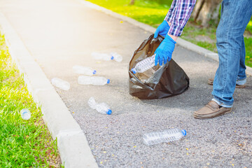 A man in a striped shirt picks up a trash bottle and puts it in a black bag on the side of the road in the park.