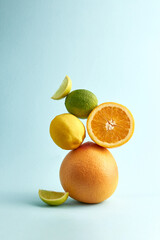 Creative balancing vertical pyramid of freshly natural fruits. Lime, lemon, grapefruit and orange on the blue color background, copy space. Conceptual healthy food. Organic citrus ingredients.