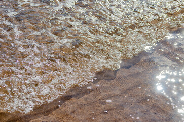 Small waves breaking with bubbles over beach selective focus motion blur background