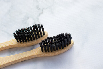 Natural bamboo toothbrush with black bristles on white marble table in bathroom. View from above....