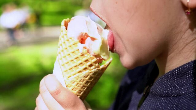 Little girl eating ice cream in waffle cone outdoors in park in sunny day. Close-up