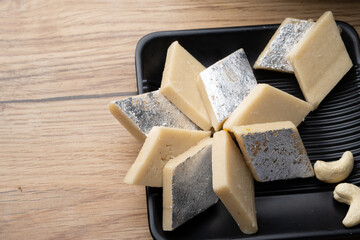 Kaju Katli is a traditional Indian Diamond shaped sweet or Mithai made using cashew paste, sugar, and mava or Khoya. served in a wooden plate over dark background. cashew barfi.