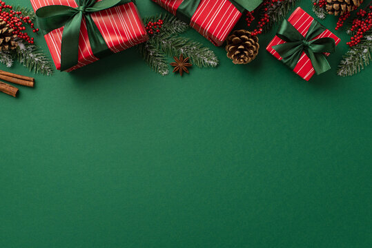 Christmas concept. Top view photo of red present boxes with green ribbon bows mistletoe berries pine cones cinnamon sticks anise and fir branches in frost on isolated green background with copyspace