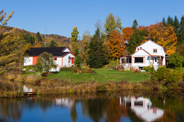 Fototapeta na wymiar Rural property with old French style orange and white house and barns set against the Laurentian mountains in colourful foliage, Stoneham-et-Tewkesbury, Quebec, Canada