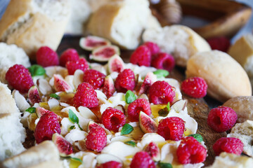 Butter board topped with fresh raspberries, figs, sliced almonds, basil leaves, and drizzled with honey. Selective focus with blurred foreground and background.