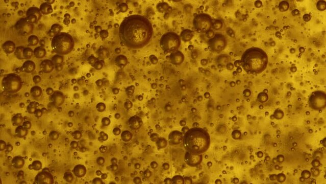 slomo macro gaseous translucent brownish bubbles rise in the yellow liquid  