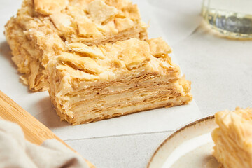 Piece of napoleon cake. Creamy vanilla slice dessert on a parchment paper. Layered baked pie. Sweet food presentation.