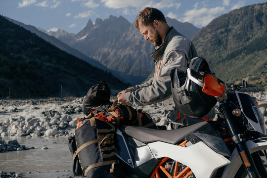 man attaching padded saddlebags for off-road motorcycle to the trunk in beautiful mountain gorge